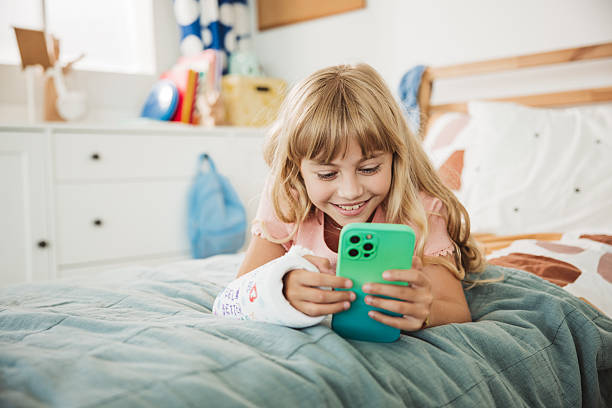 istock Cute girl with a broken arm in orthopedic cast using smartphone 2231709607