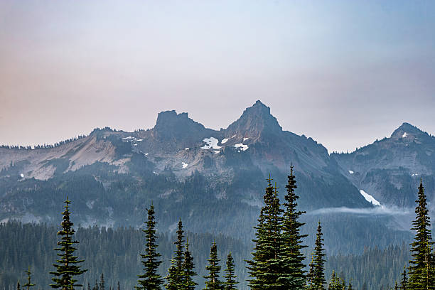 istock A striking alpine scene with rugged mountain peaks, scattered snow patches, and dense evergreen forest under a hazy sky. Perfect for themes of wilderness, nature, travel, hiking, and outdoor adventure. 2231715329