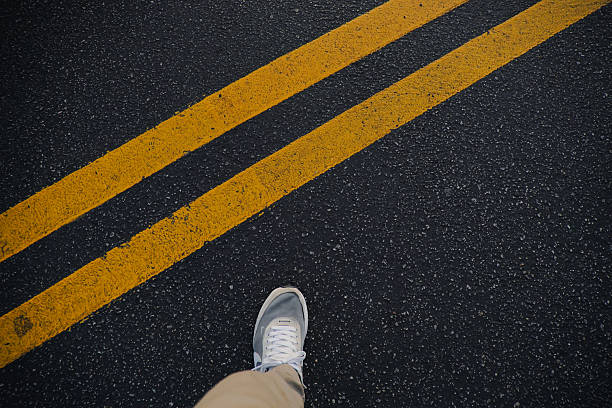 istock Dark road asphalt with double yellow line and shoe foot composition 2231716442