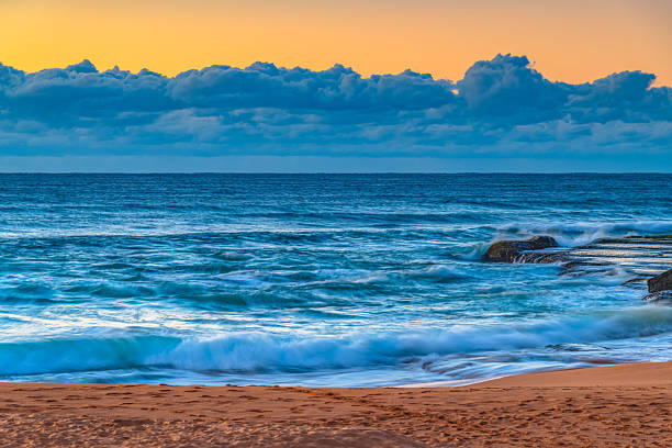 Sunrise seascape with low cloud bank and waves at Bilgola Beach on the Northern Beaches of Sydney, NSW, Australia.