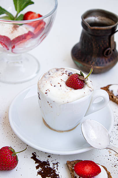 Bright tabletop still life: vanilla ice cream with strawberries and mint, a foamy espresso brewed in a cezve, and crunchy toasts with cream and berries on a white background