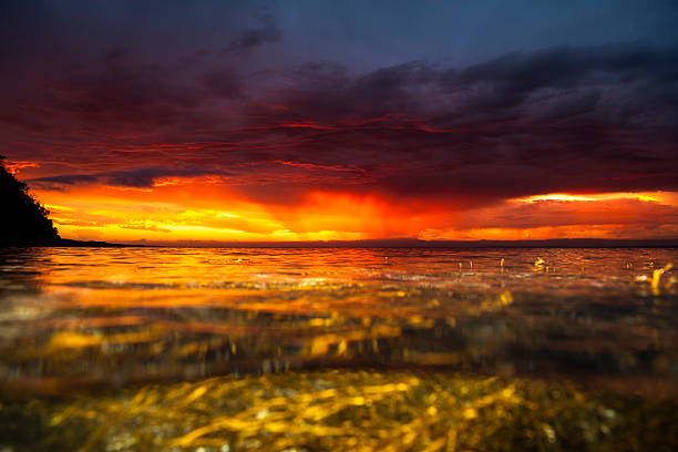 Sunset over Jervis Bay, Australia, with dramatic golden light reflecting on the ocean surface beneath stormy red and purple clouds.