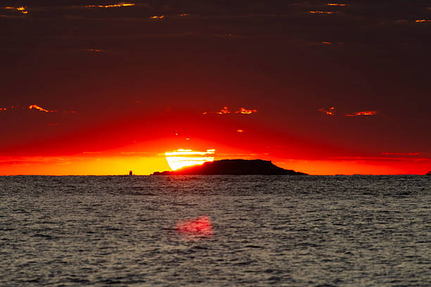 Dramatic sunrise behind a small island in Port Stephens, Australia, with vibrant red and orange skies reflecting over the calm ocean.