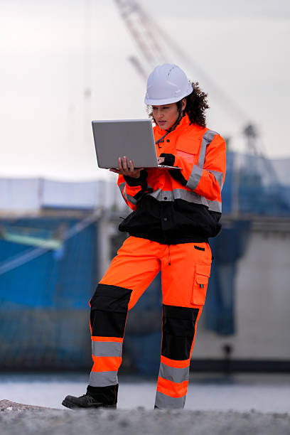 istock Two port engineers in high-visibility orange uniforms and hard hats communicate while inspecting dockside logistics using a laptop and walkie-talkie, symbolizing teamwork and safety. 2231740177