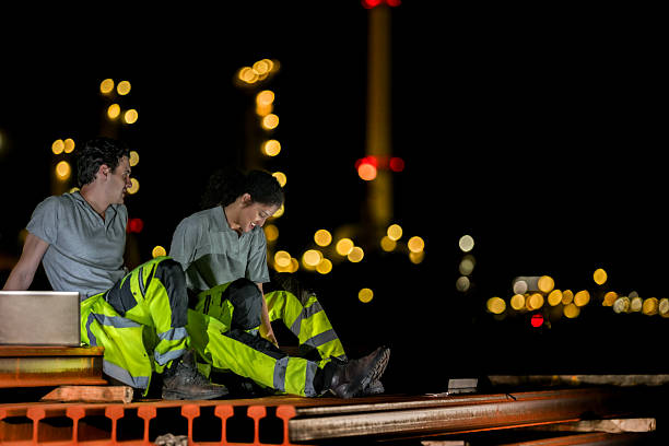 istock Two industrial workers take a break during the night shift at a construction site, sitting on steel beams with city lights in the background, showing fatigue and camaraderie. 2231741472