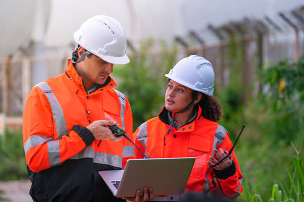 istock Two engineers in high-visibility safety gear and hard hats discuss project plans on a laptop in front of large spherical gas storage tanks at an industrial coastal facility. 2231741733
