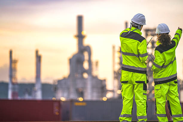 istock Two engineers in high-visibility suits and helmets review data on a tablet while standing in front of a refinery at sunrise, indicating teamwork and safety in a heavy industry zone. 2231742099