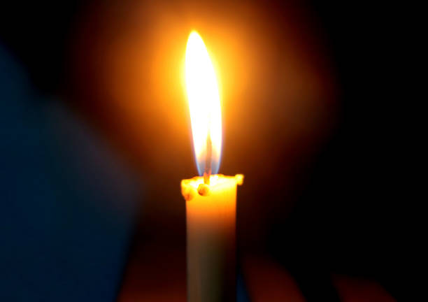 Burning candle standing on a windowsill late in the evening night.