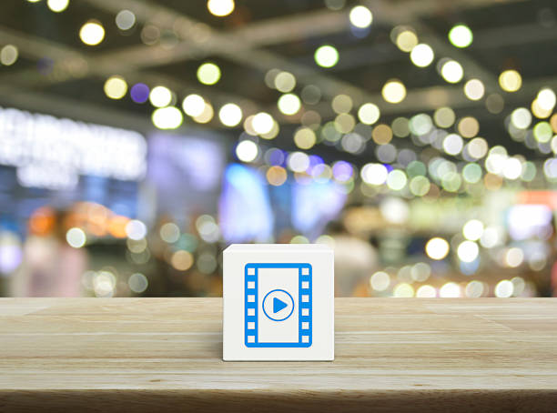 Play button with movie flat icon on white block cube on wooden table over blur light and shadow of shopping mall, Business cinema online concept