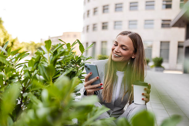 istock Smiling woman using phone and coffee cup in front of office complex 2231764292