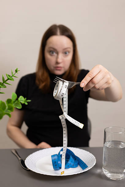 istock Person Shows Fork With Measuring Tape Instead of Food at Dining Table During Diet Reflection 2231767019