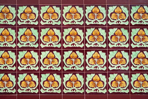 Close-up of vintage ceramic wall tiles with ornate floral pattern in yellow and green on a maroon background. Traditional decorative tile design with symmetry and texture.
