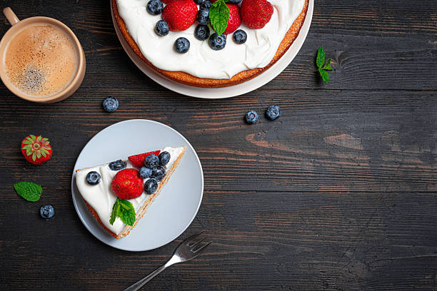 Sponge cake with cream cheese and fresh summer berries on wooden, top view, copy space. Piece of cake with whipped cream, strawberries and blueberries and coffee.