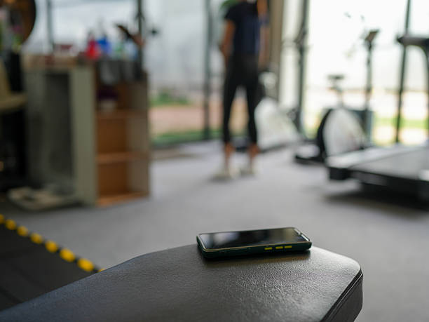 istock Smartphone rests on gym bench, with blurred figure in background engaged in workout. scene captures modern fitness environment, emphasizing health and activity 2231774688