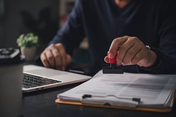 istock Businessman stamping approval on contract document at office desk with laptop, validating legal agreement for business deal, contract management and authorization concept. 2231779545