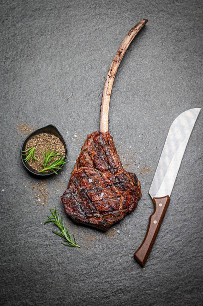 istock Grilled Tomahawk Steak with Herbs and Knife on Stone Background 2231785475