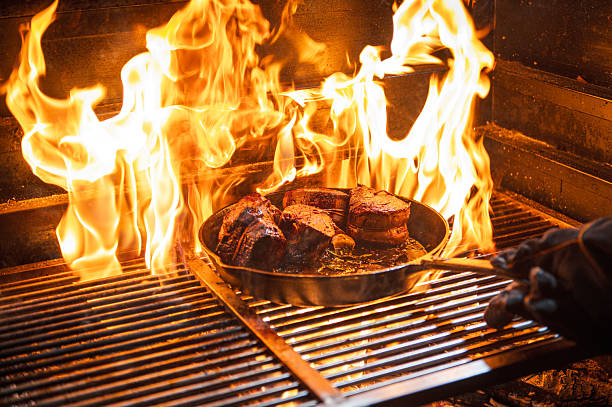 A sizzling filet mignon in a pan searing over intense open flames on a professional grill. This image captures the essence of culinary expertise, hearty meals, and the vibrant energy of a barbecue setting.