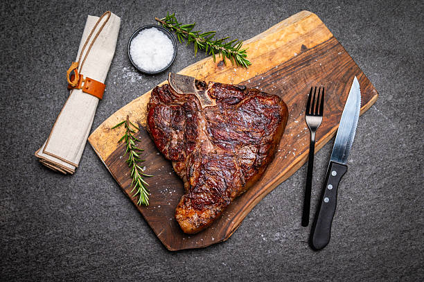 Grilled T-Bone Steak on Wooden Board with Rosemary and Fork