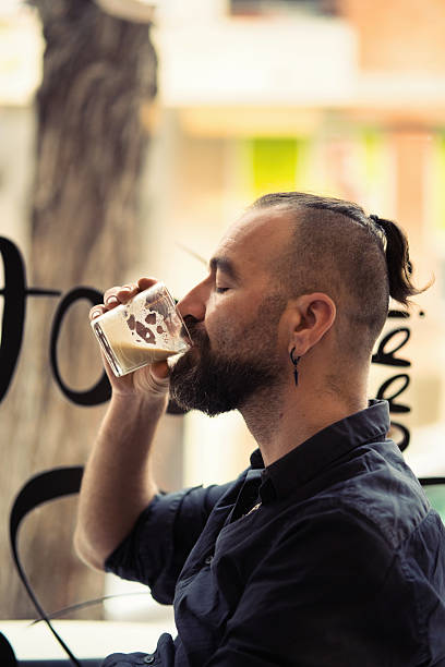 Potrait of young man in casual outfit drinkig cool beer, posing isolated over light blue studio background. Feeling relaxed. Concept of youth, fashion, lifestyle, emotions. Copy space for ad