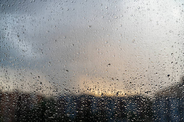 Raindrops cover a window, revealing a dramatic sunset and stormy clouds