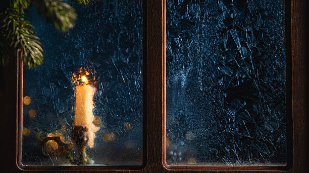 istock Single white candle is burning behind a frozen window during a cold winter night, creating a warm and cozy atmosphere with the fir tree branch in the foreground 2231811885