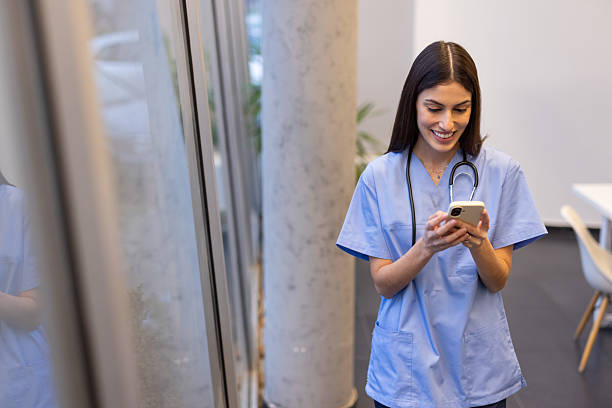 istock Professional female physician wearing blue scrubs, checking smartphone while walking through bright medical facility hallway 2231816082