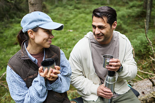 istock Young Caucasian Man and Woman Smiling While Drinking Outdoors in Forest 2231817981