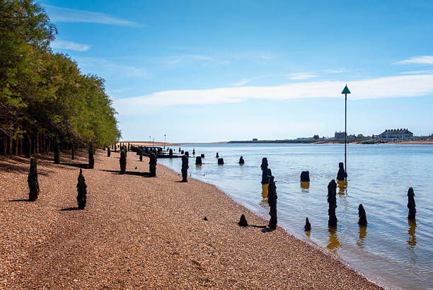 A young black girl stands at the edge of the sea, while her younger sister plays nearby and a women sleeps in the sun on Southend-on-Sea beach, Essex, UK.