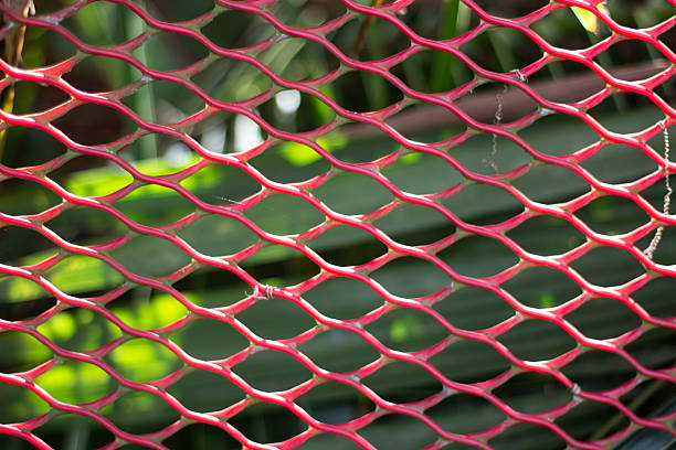 A detailed close up showcases the intricate red mesh pattern, its geometric openings revealing a softly blurred green background with hints of foliage and light.
