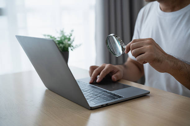istock Close-Up of a Person Using a Laptop Computer with a Magnifying Glass in a Modern Workspace Setting with Natural Light and Indoor Plant 2231827292