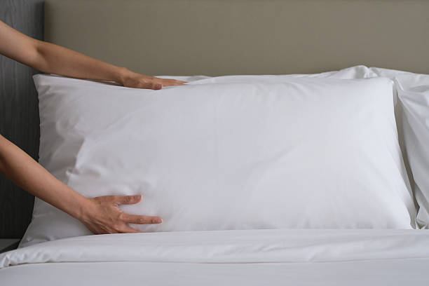 istock Hands placing a large white pillow on a neatly made bed during housekeeping. 2231828844