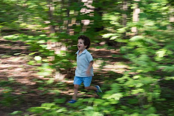 Little boy running on dirt road in forest among trees.