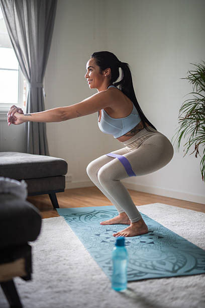 istock Side view of female doing squats with weight training elastic band on exercise mat in her living room. 2231832967