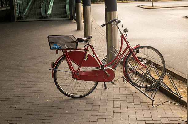 Classic red dutch bicycle parked against an empty metal bike rack on a brick paved street