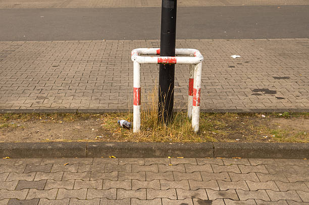 Lamppost featuring a protective barrier stands on a sidewalk with a discarded bottle nearby, highlighting urban neglect