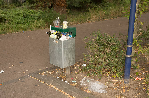 Overflowing trash can and surrounding litter polluting a public park, highlighting environmental issues and irresponsible waste disposal