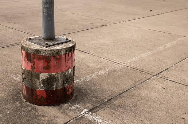 Close-up of weathered concrete pole base featuring red and white stripes, standing on a cement surface in parking area