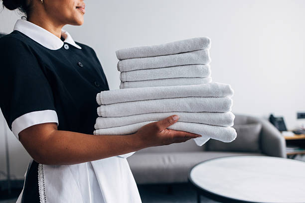 Professional hotel staff dressed in a black uniform holds a stack of freshly folded white towels, symbolizing cleanliness and excellent hospitality in a clean and modern interior setting.