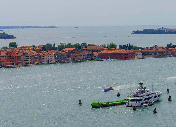 Panoramic view of San Giorgio Maggiore island and the Venetian lagoon, with historic buildings, church tower, and boats crossing the water.