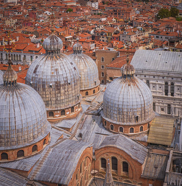 A captivating view of St. Mark's Square in Venice, Italy, showcasing the grandeur of the historic piazza. The square is flanked by the majestic St. Mark's Basilica, the towering Campanile, and the elegant arcades of the Procuratie buildings. The lively atmosphere is filled with visitors, outdoor cafes, and pigeons, epitomizing the heart of Venice's cultural and social life.