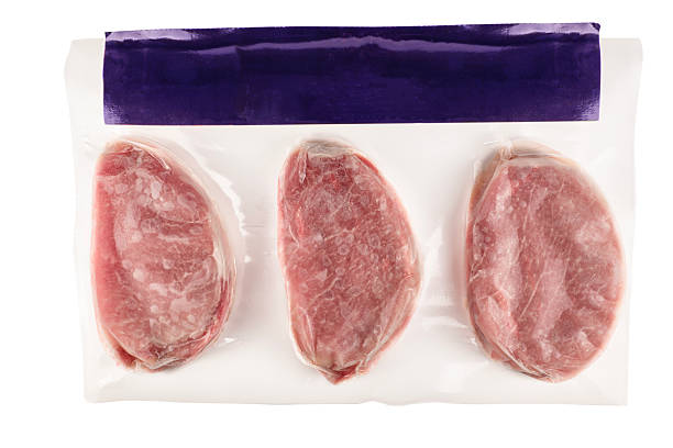 Vacuum-packed raw pork chops sealed in plastic wrap on a white background.