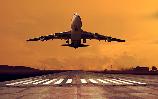 A jet airplane takes off during a vibrant orange sunset, silhouetted against the glowing sky, captured from a low angle.