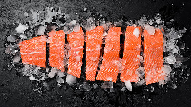 istock Fresh raw salmon fillet on ice. Fish steak on black stone background. Top view. 2231856080