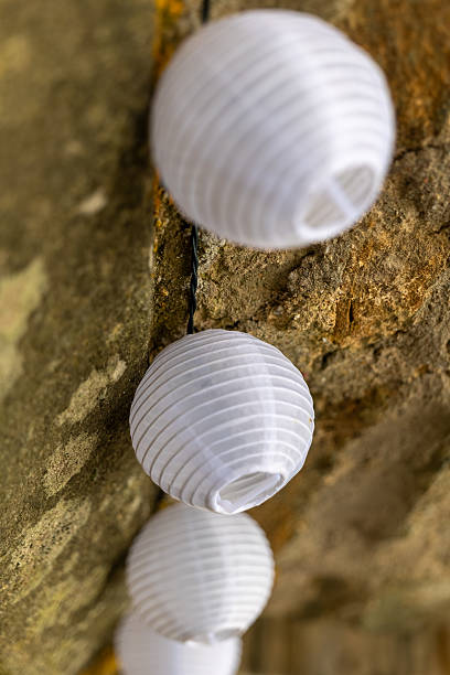 Delicate white lanterns adorn a stone wall, creating a whimsical ambiance in the evening light