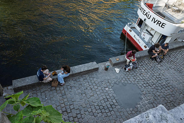 Friends relaxing on a cobblestone quay by the Seine River in Paris, with a boat moored nearby.