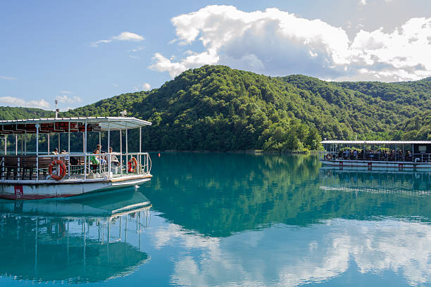 Plitvice Lakes, Croatia – July 9th 2025 – Tourist boats with passengers on turquoise lake surrounded by forested hills at Plitvice Lakes National Park. Editorial use only.