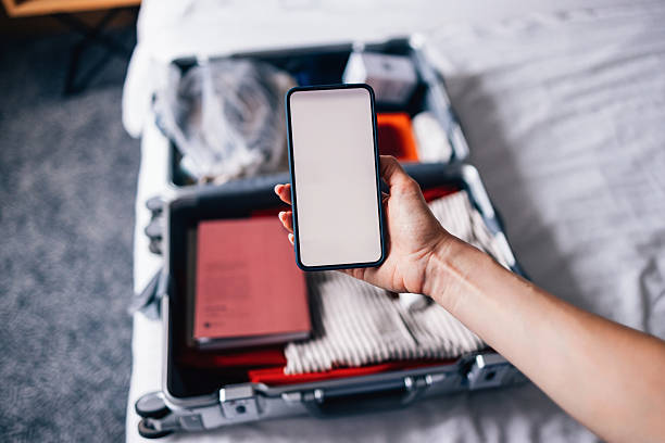 istock Hand Holding Smartphone Above Open Suitcase Prepared for Travel 2231869319