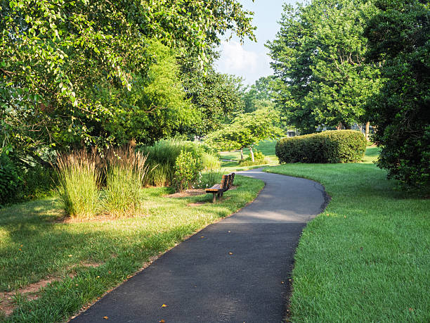 istock Winding paved path through a green park with a bench in Ashburn Village, Virginia 2231874392