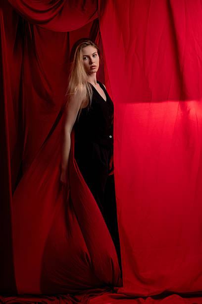 istock Model poses dramatically behind red curtain fabric in soft lighting at an indoor studio during a photoshoot 2231877081