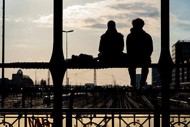 istock Silhouette of two people chatting on a bridge over the train tracks. 2231877628